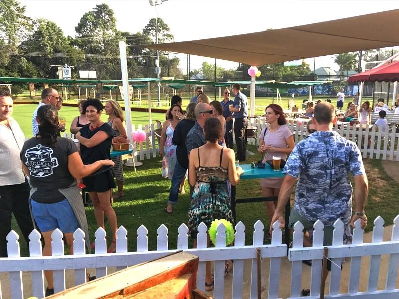 A crowd gathered on the lawn beside the green for a function, with bunting and a white picket fence