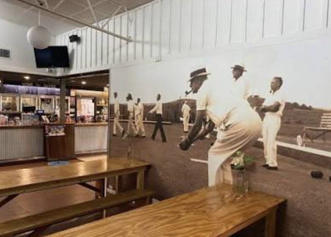 Inside the Bowlo: timber tables in front of a large vintage mural of bowlers on the green